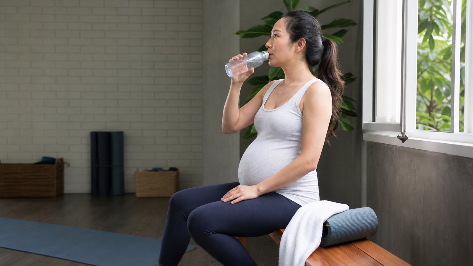 Pregnant woman hydrating in a cool yoga studio to reduce overheating risk