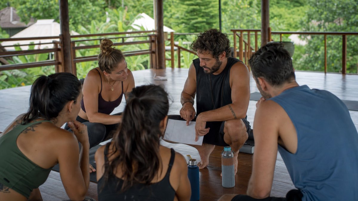 Hot yoga teacher training group reviewing hydration, safe room practice, and program red flags with a trainer in an open Bali studio