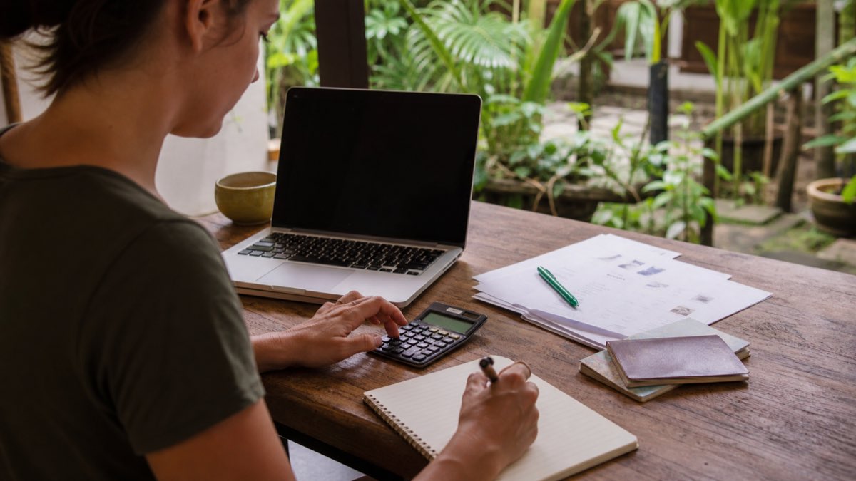 Yoga trainee uses a calculator, laptop, passport, and notebook to review the complete YogaFX Bali teacher training budget