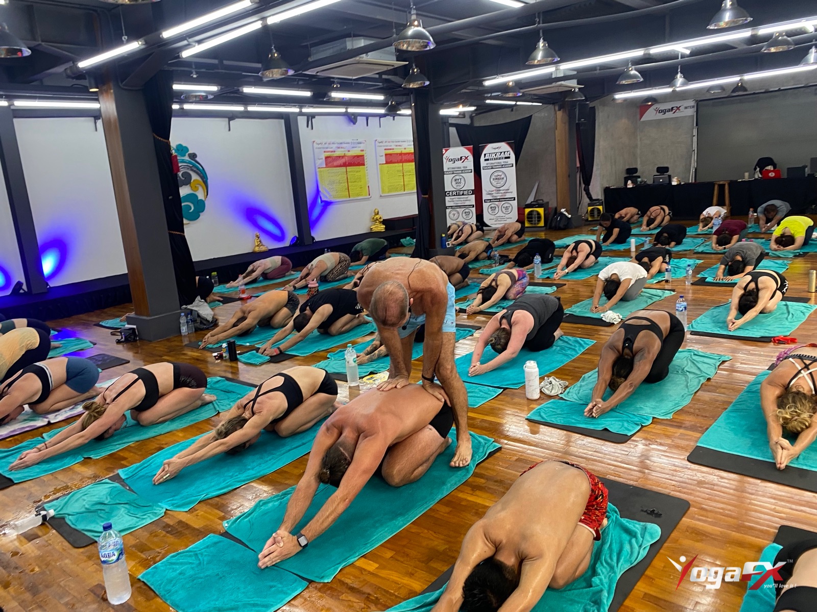 Instructor adjusting a student in child's pose, the kind of coaching that decides hot yoga vs Pilates for many men