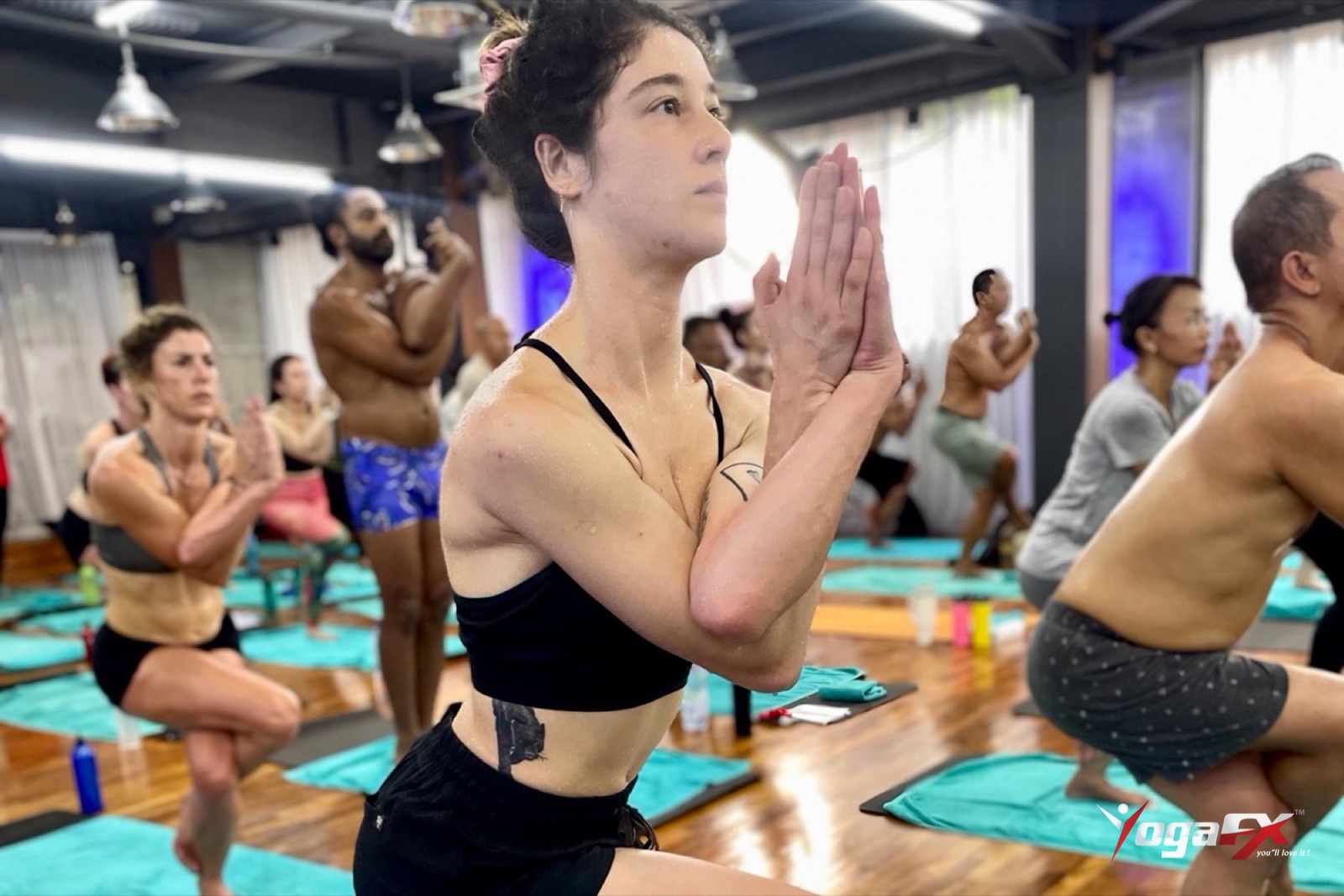 Male and female students in prayer pose during the standing series of a hot yoga teacher training class