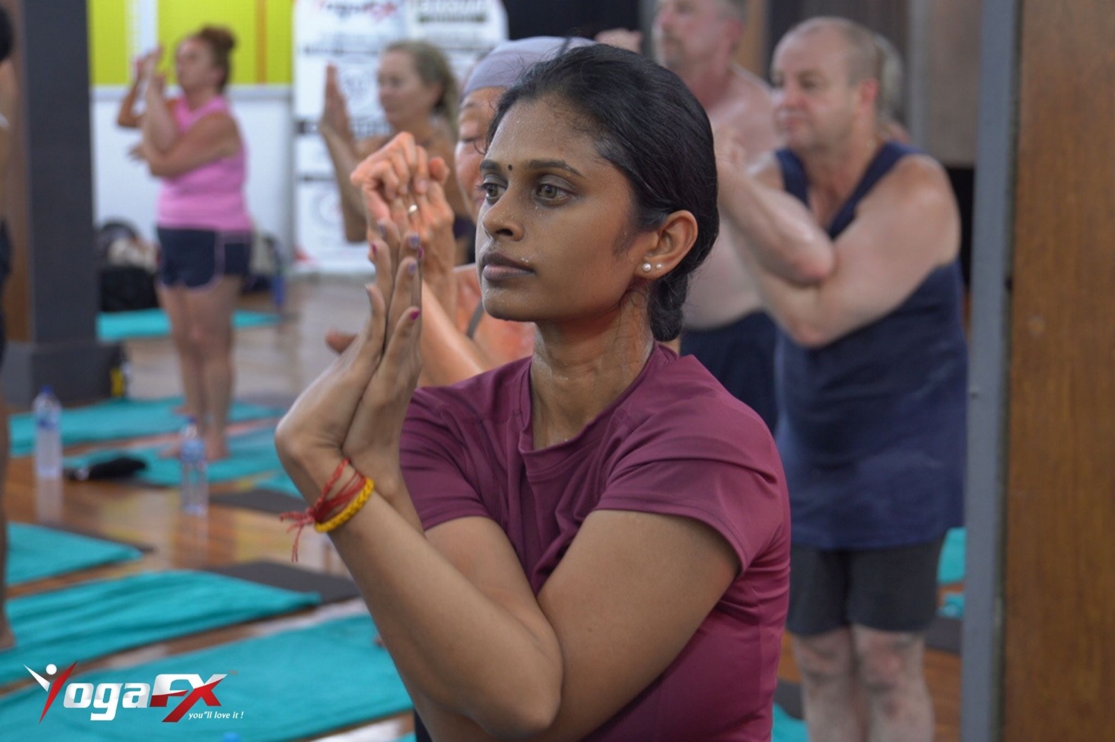 Men's hot yoga class cueing: students of both sexes hold eagle pose in the heat while sweat beads on their faces